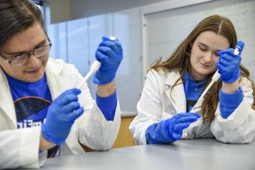 学生s Nathan Rice, 24岁 和 Lexi Lumley, 24岁 conduct research in labcoats 和 blue gloves.